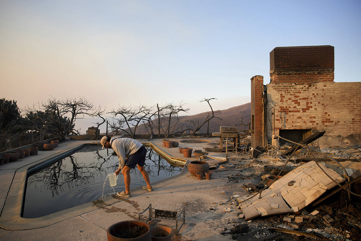 Garrett Yost gathers water from a pool while surveying his neighbors' fire-ravaged properties i ...