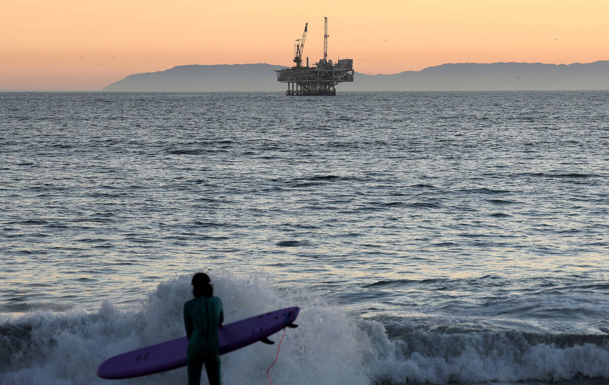 A surfer stands with offshore oil and gas platform Esther in the distance on Sunday, Jan. 5, 20 ...