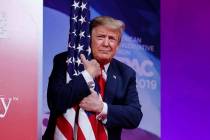 President Donald Trump hugs the American flag as he arrives to speak at Conservative Political ...