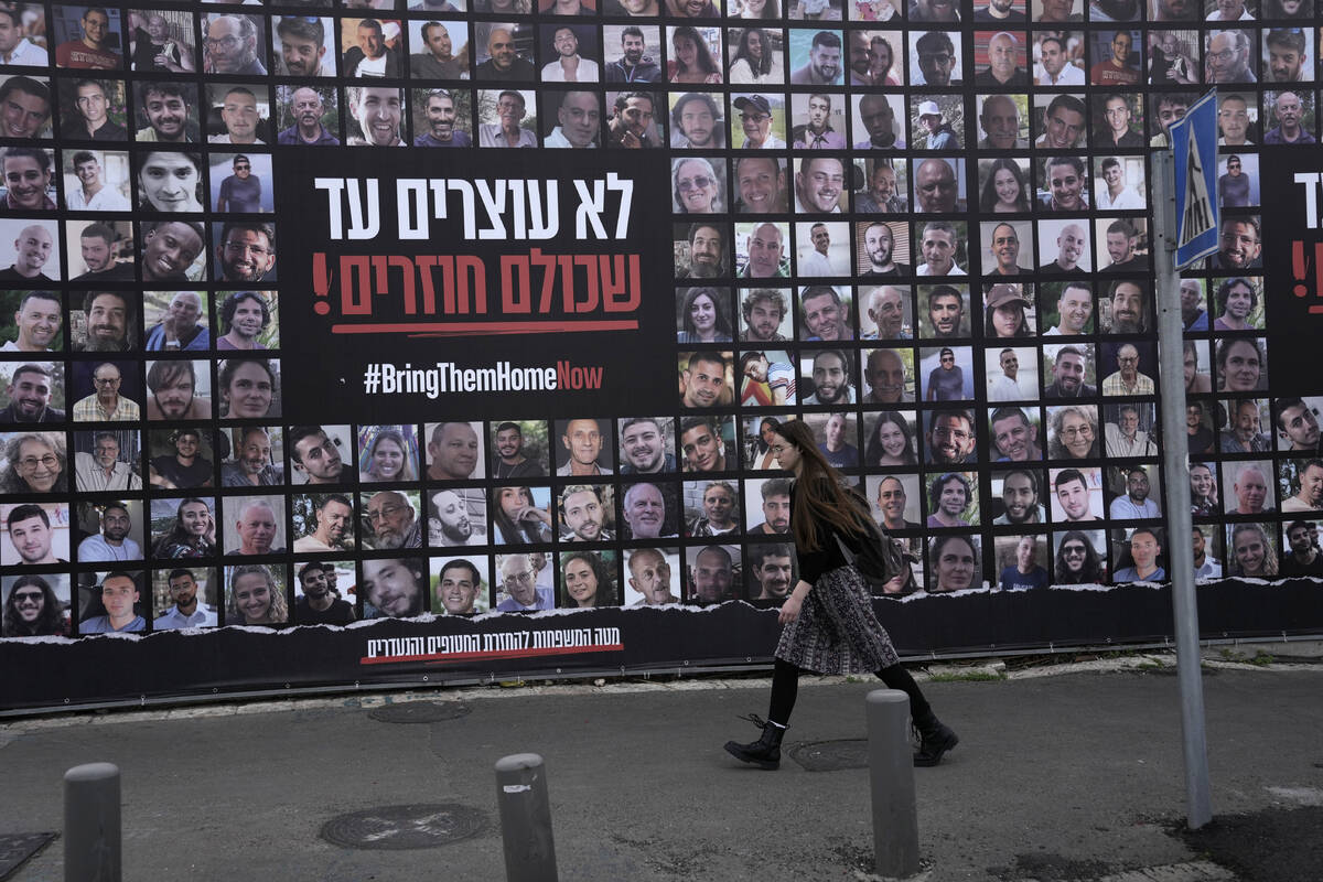 A woman walks past photos of hostages held by Hamas in the Gaza Strip, in Jerusalem, Friday, Ja ...