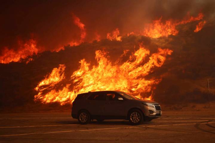 A vehicle rides past a hillside engulfed in flames caused by the Hughes Fire in Castaic, Calif. ...