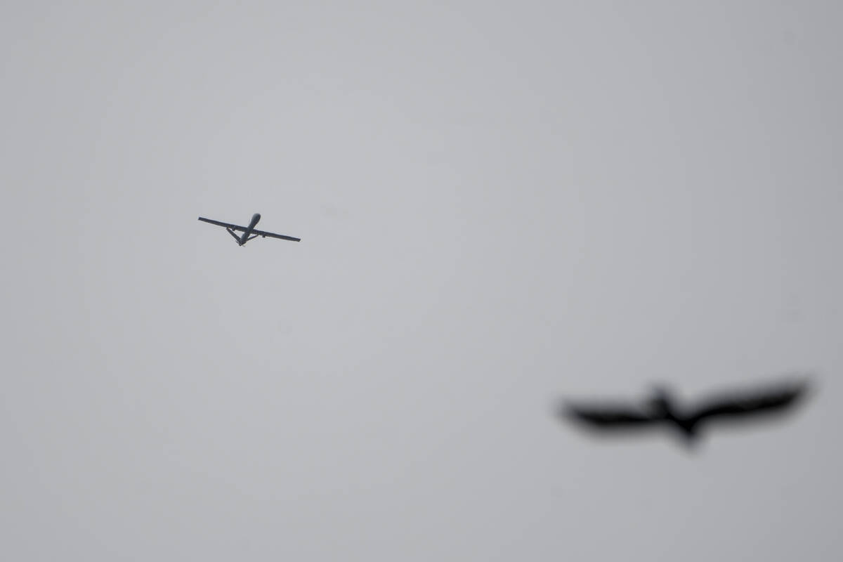 An Israeli drone flies while Israeli military vehicles guard a road where a military bulldozer ...