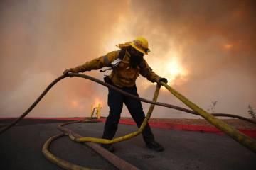 A firefighter sets out fire hoses to fight the Hughes Fire in Castaic, Calif., Wednesday, Jan. ...