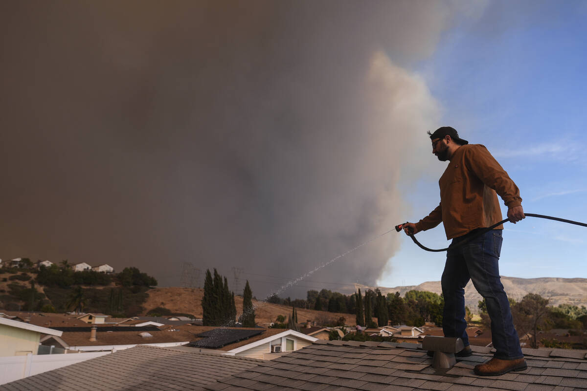 Andrew Aguilar spray water from the top of the roof at his brother's home Castaic, Calif., as a ...