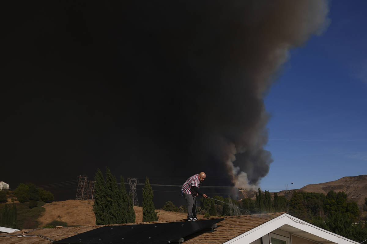 A home owner sprays water from the top of the roof in Castaic, Calif., as a large plume of smok ...