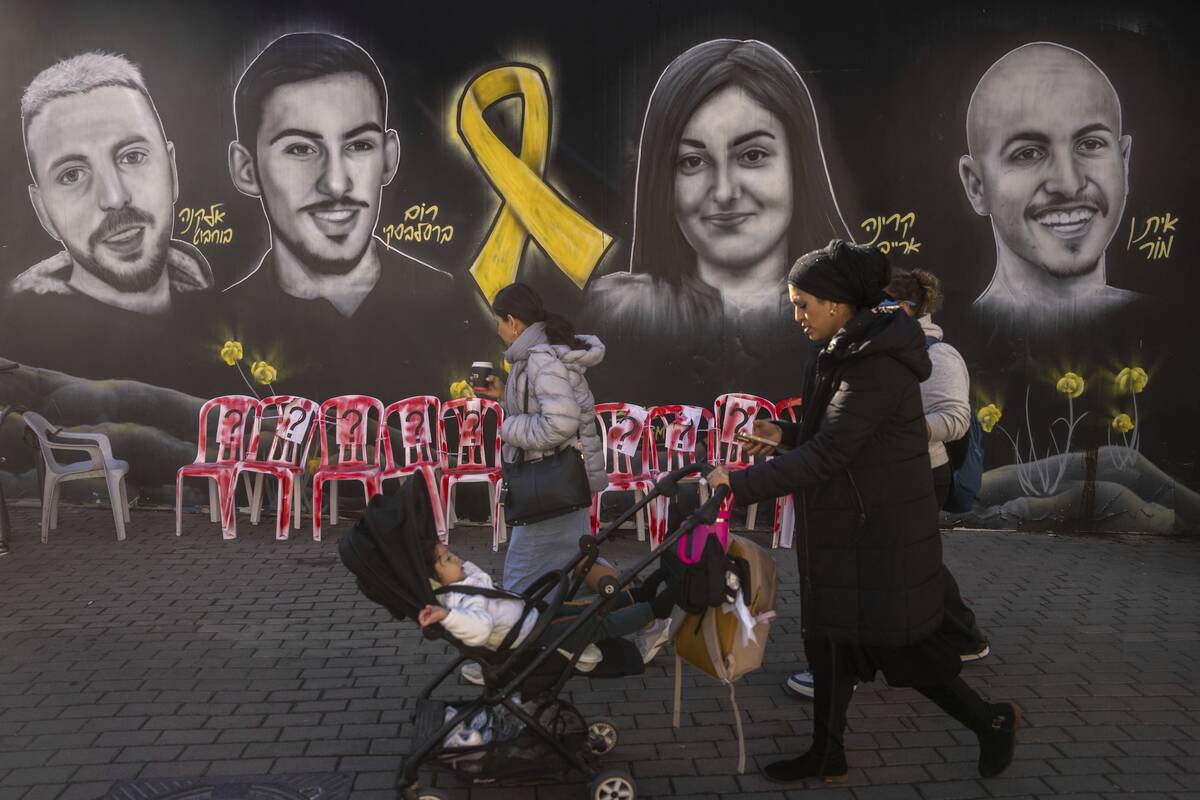 An ultra-Orthodox Jewish woman walks past an installation, and a mural of portraits of hostages ...