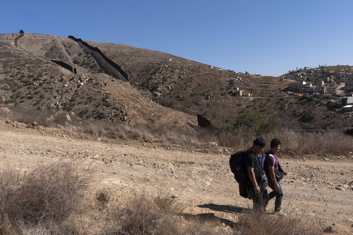 Two men walk down a road towards Border Patrol agents after crossing the border illegally throu ...