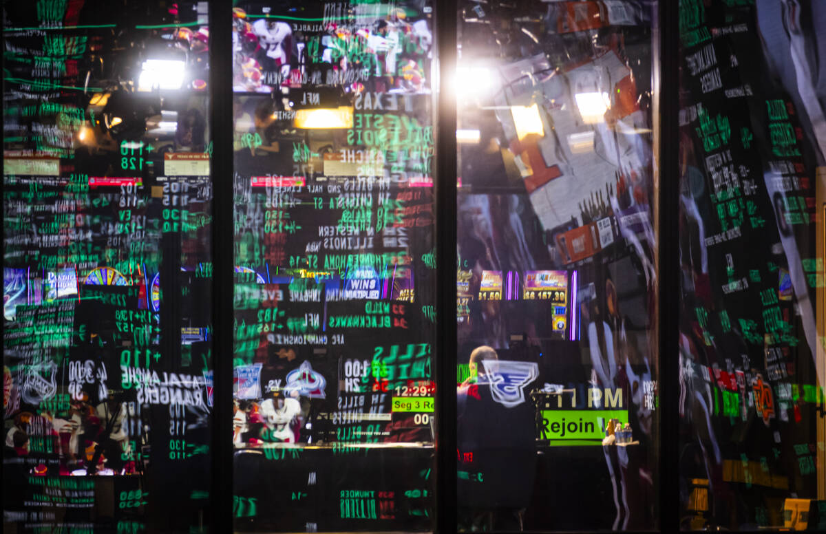 Betting lines are reflected in glass as people watch the NFC championship football game between ...