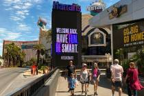 FILE - Visitors walk along the Las Vegas Strip with a sign for Harrah's saying they are open fo ...