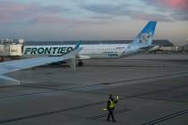 A ground crew member directs a plane back from a gate near a Frontier Airlines jet at Harry Rei ...