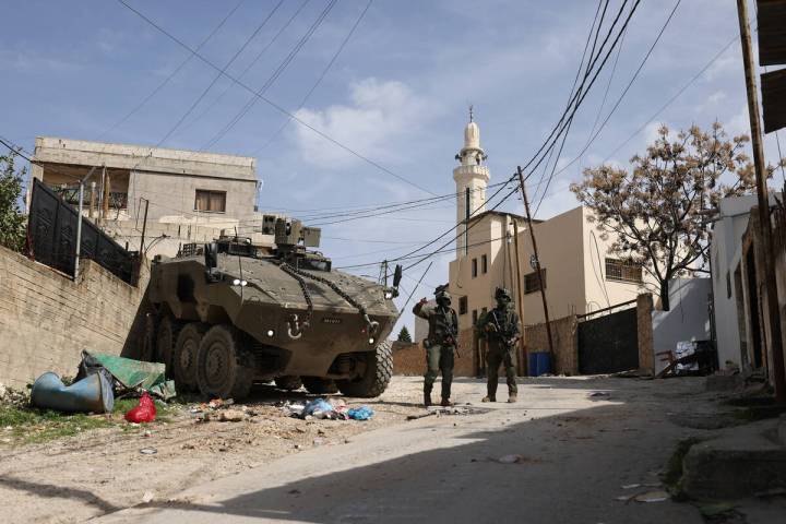 Israeli soldiers stand guar near their armoured vehicles as they conduct a raid in the eastern ...